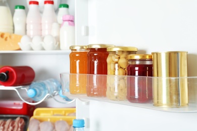 Jars with preserves and tin can on refrigerator door shelf, closeup