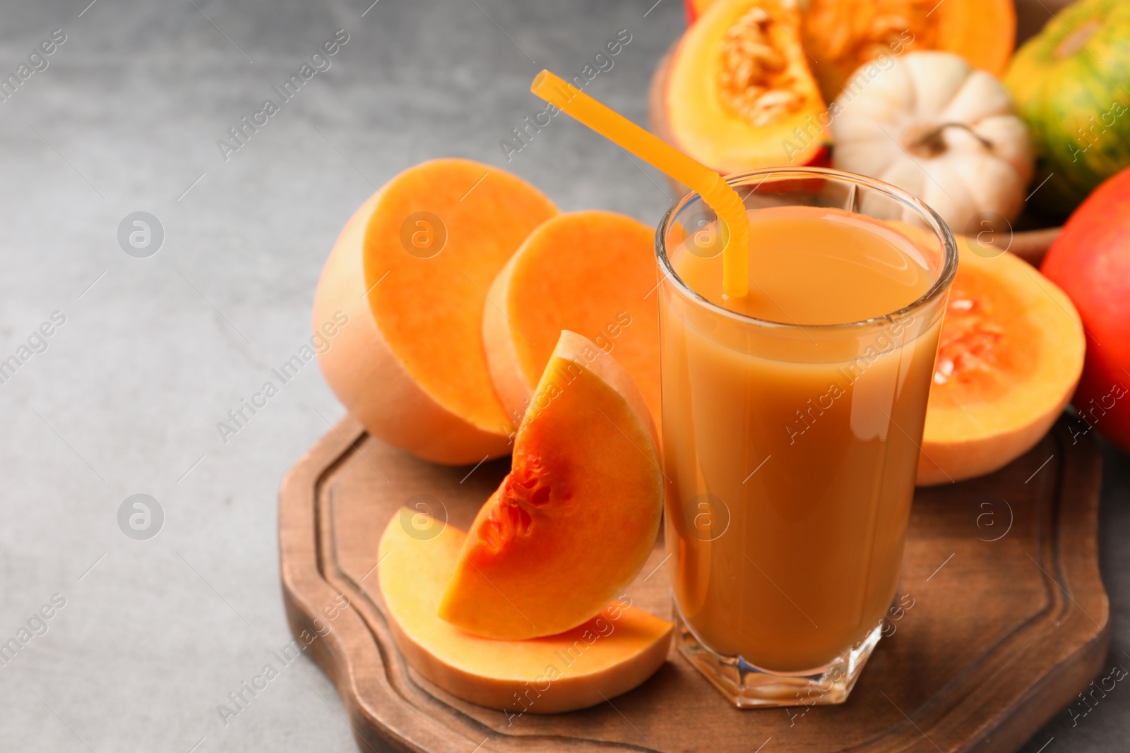 Photo of Tasty pumpkin juice in glass and different pumpkins on light grey table. Space for text