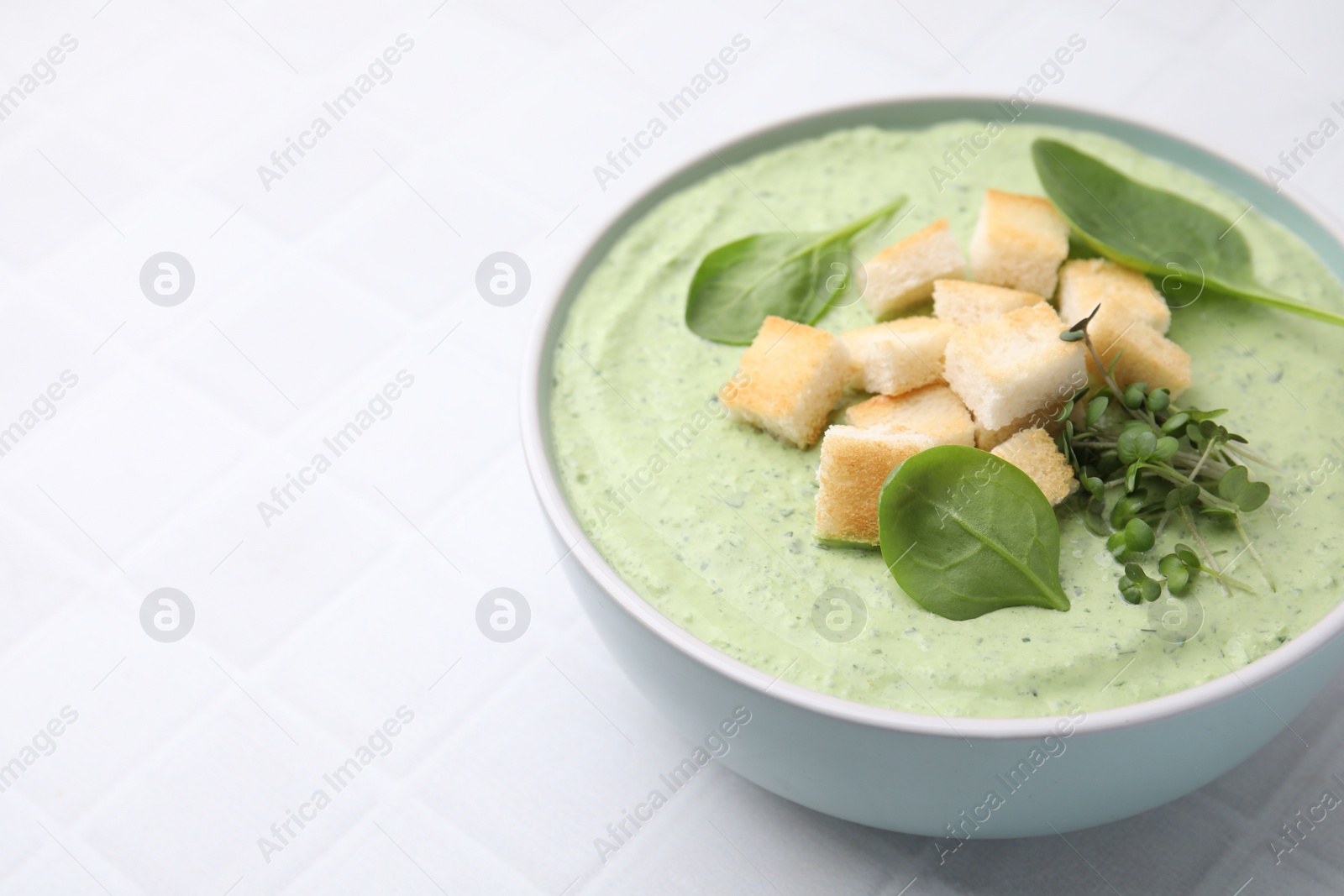 Photo of Delicious spinach cream soup with croutons in bowl on white tiled table. Space for text