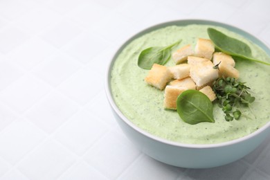 Delicious spinach cream soup with croutons in bowl on white tiled table. Space for text