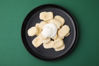 Photo of Plate of tasty lazy dumplings with sour cream on dark green background, top view