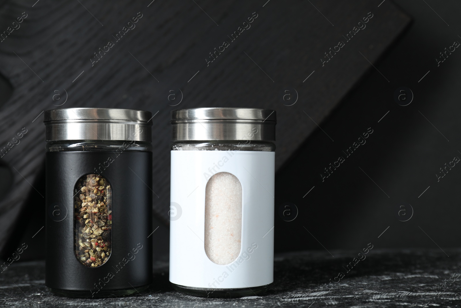 Photo of Salt and pepper shakers on dark table. Space for text