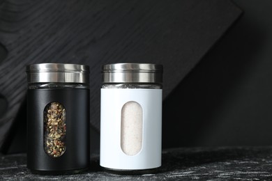 Salt and pepper shakers on dark table. Space for text