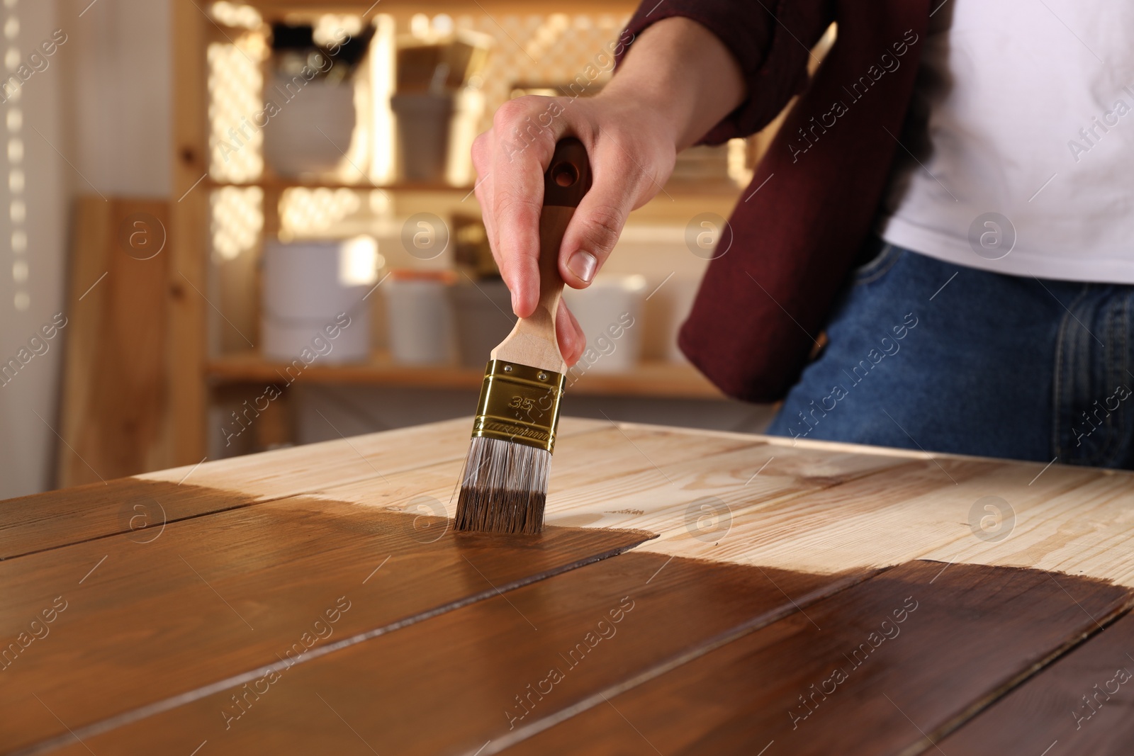 Photo of Man with brush applying wood stain onto wooden surface indoors, closeup