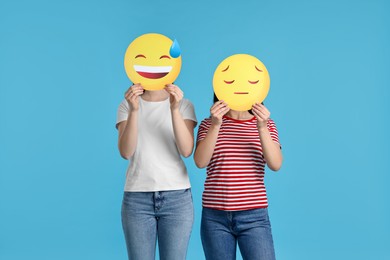 Photo of People covering faces with emoticons on light blue background