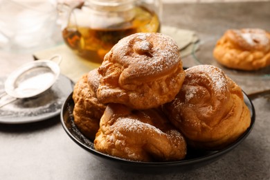 Photo of Delicious profiteroles with powdered sugar in bowl on grey table