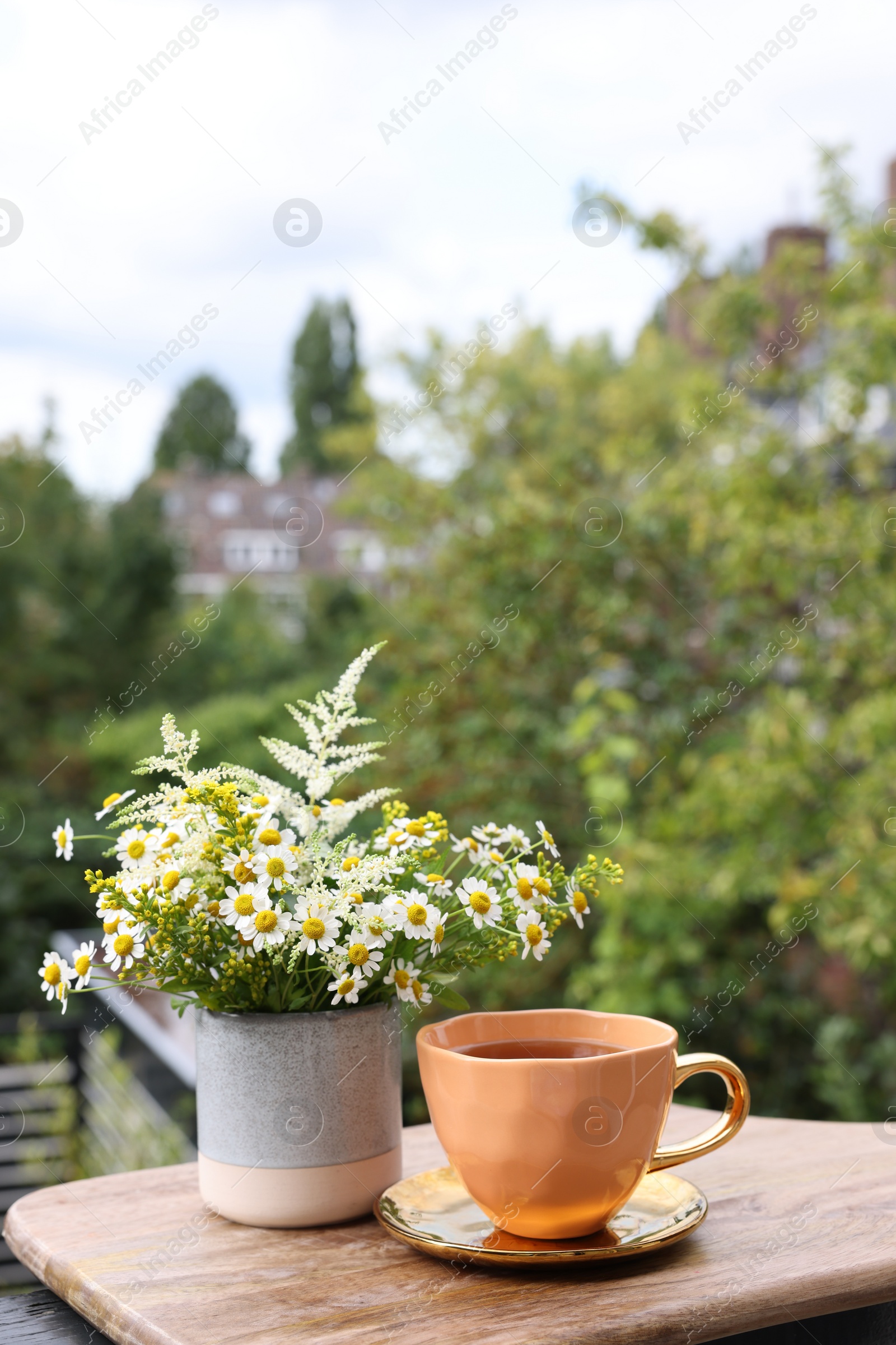 Photo of Cup of delicious chamomile tea and fresh flowers outdoors