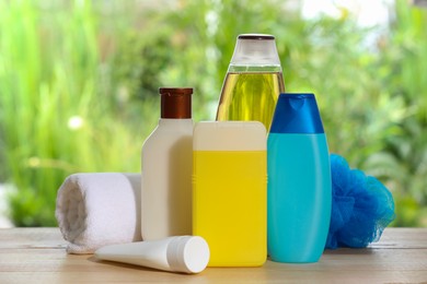 Photo of Different shower gel bottles with towel and mesh pouf on wooden table