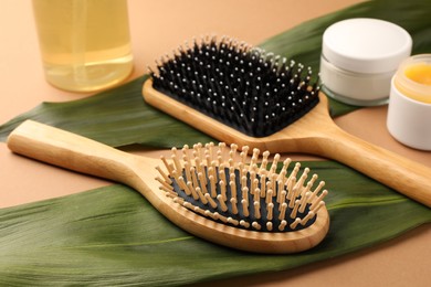 Photo of Wooden hairbrushes, different cosmetic products and green leaves on light brown background, closeup