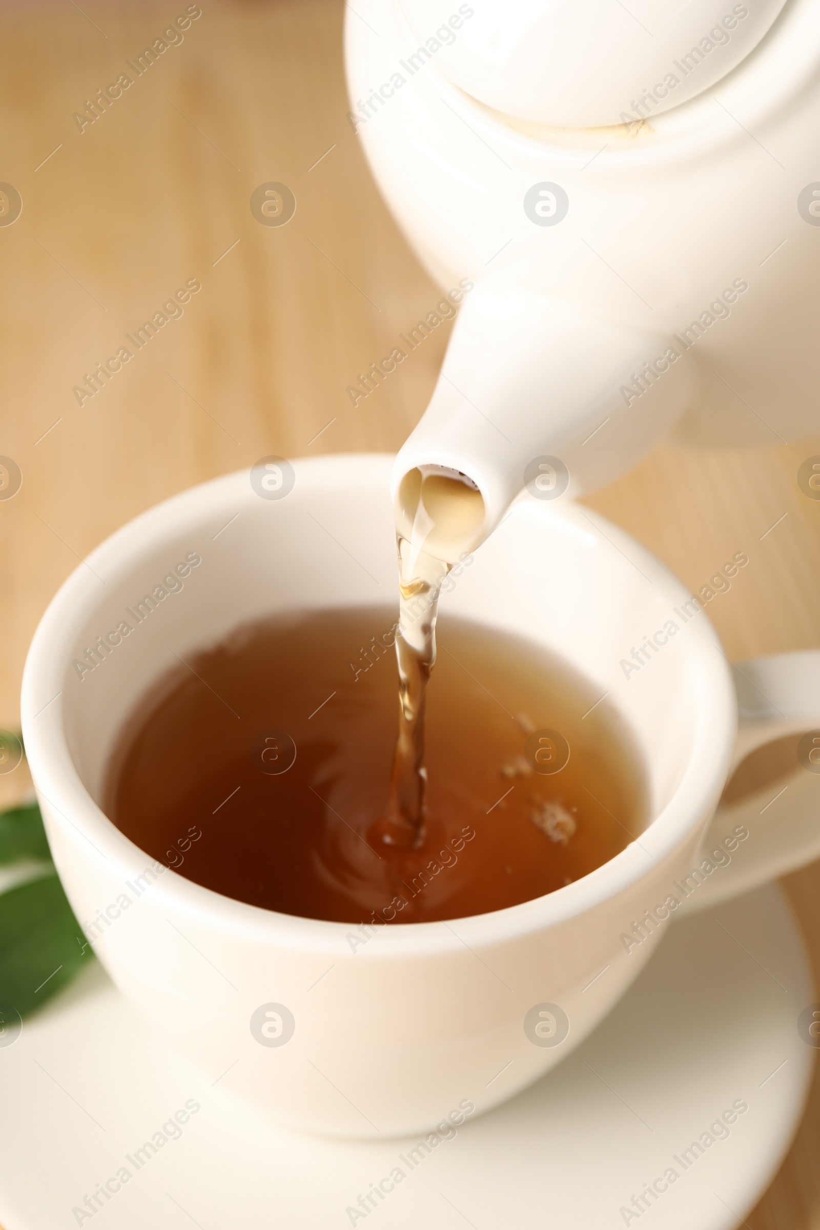 Photo of Pouring tasty tea into cup at table, closeup