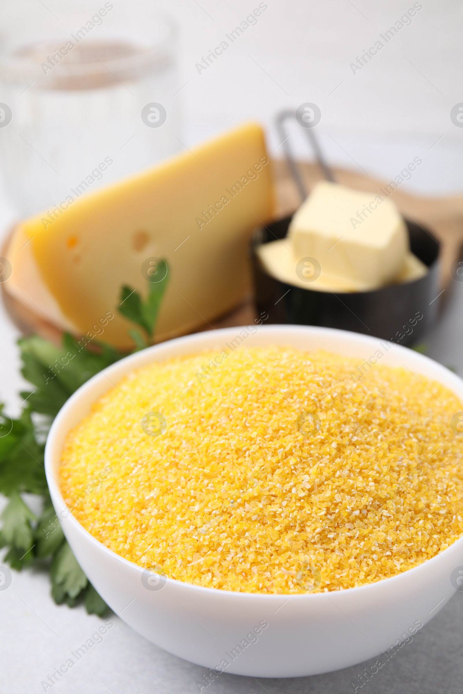 Photo of Raw cornmeal in bowl, parsley, cheese and butter on light table, closeup