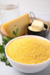 Photo of Raw cornmeal in bowl, parsley, cheese and butter on light table, closeup