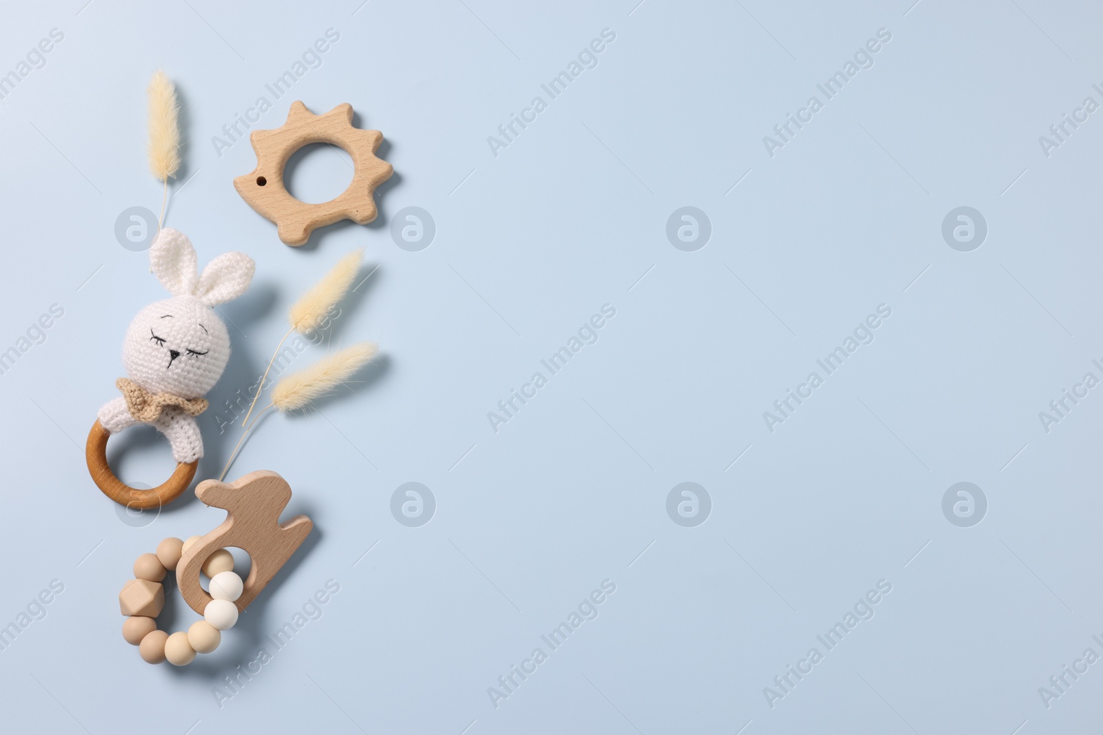 Photo of Baby accessories. Rattle, teethers and dry spikes on light blue background, flat lay. Space for text