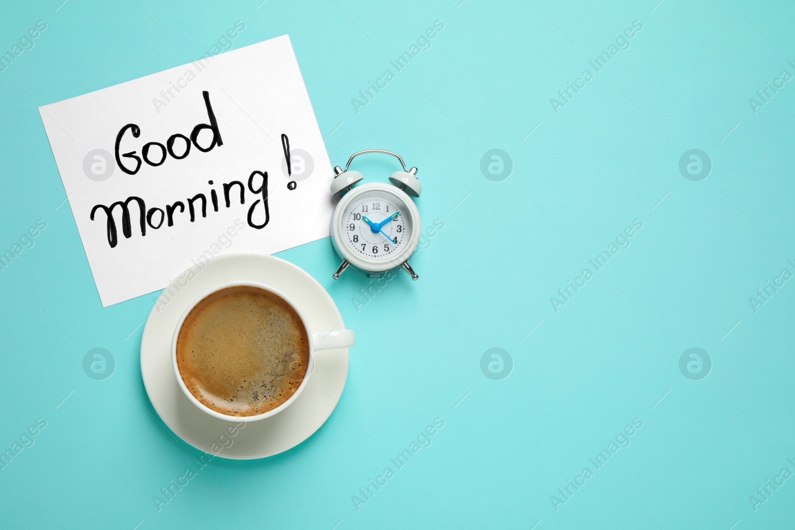 Photo of Delicious coffee, alarm clock and card with GOOD MORNING wish on light blue background, flat lay. Space for text