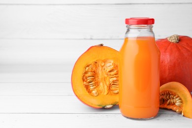 Photo of Tasty pumpkin juice in glass bottle, whole and cut pumpkins on white wooden table. Space for text