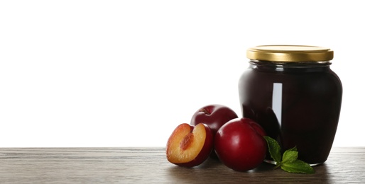 Glass jar of pickled plums on wooden table against white background, space for text