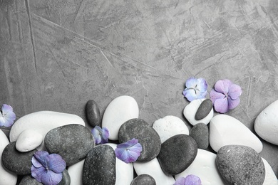 Zen stones and exotic flowers on grey background, top view with space for text