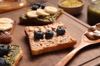 Photo of Toasts with different nut butters, banana slices, blueberries and nuts on wooden board, closeup