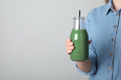 Woman holding bottle with spirulina smoothie on grey background, closeup. Space for text