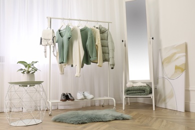 Photo of Rack with stylish warm clothes and shoes near mirror in dressing room