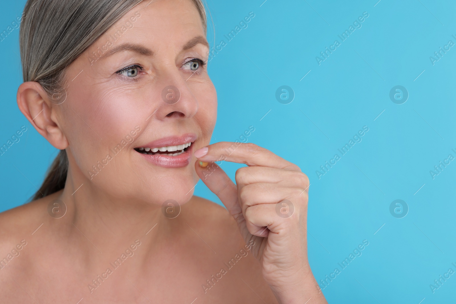 Photo of Beautiful woman taking vitamin pill on light blue background, space for text