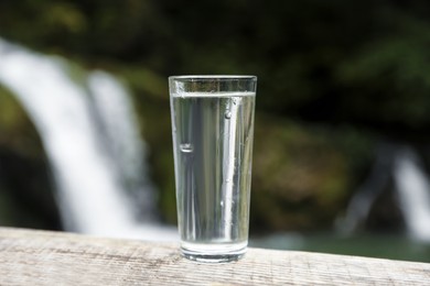 Photo of Glass of water on wooden surface near waterfall outdoors