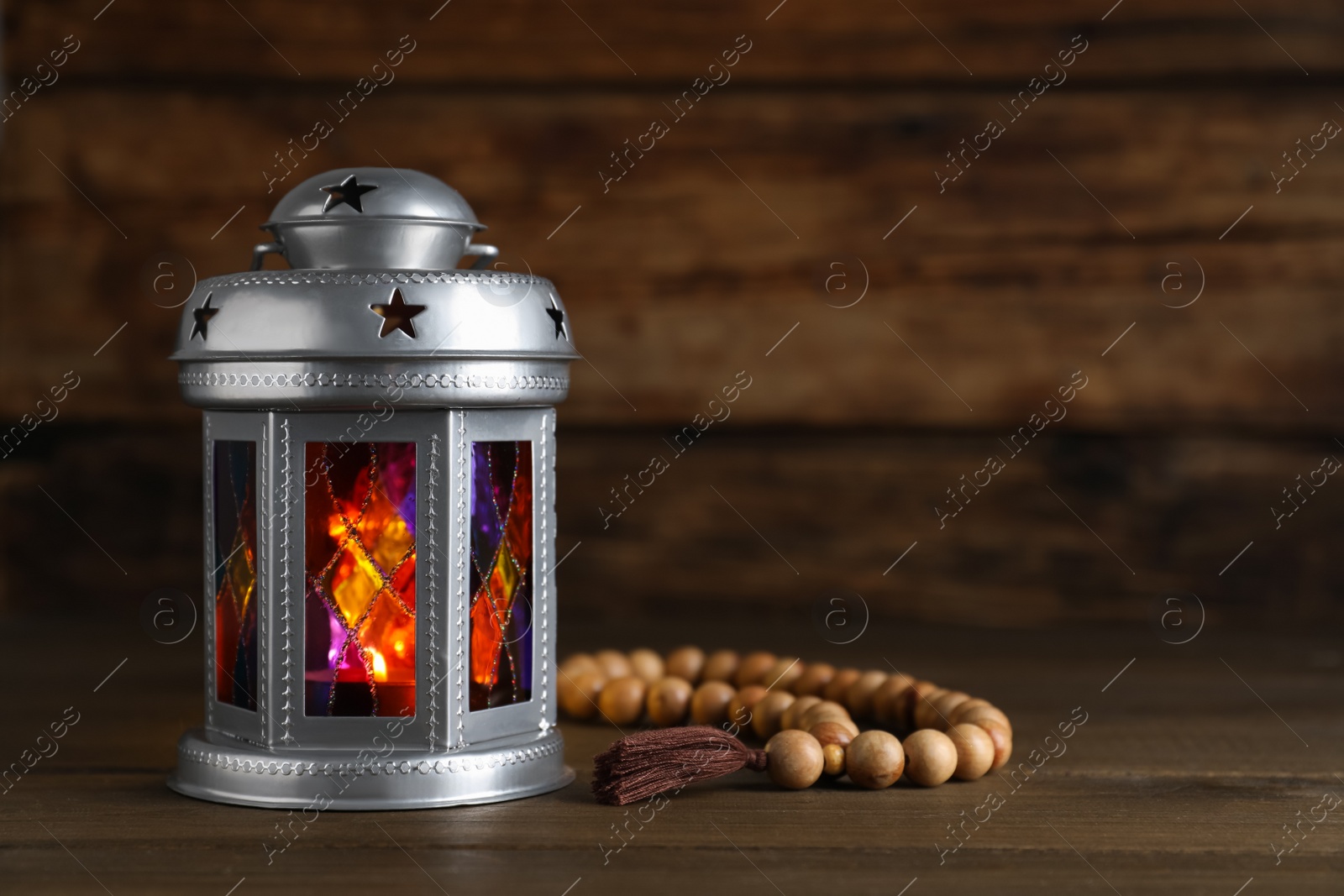 Photo of Decorative Arabic lantern and prayer beads on wooden table. Space for text