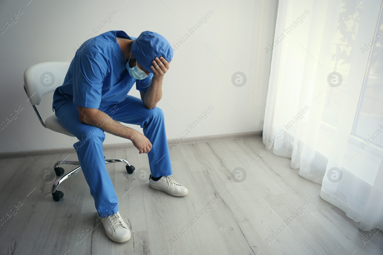 Photo of Exhausted doctor sitting on chair indoors, space for text. Stress of health care workers during COVID-19 pandemic