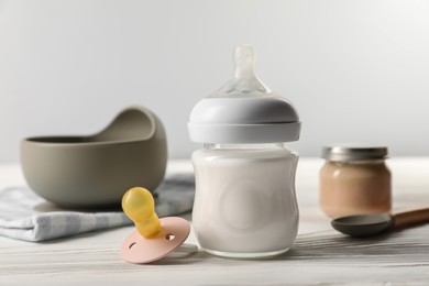 Photo of Bottle of milk and pacifier on white wooden table