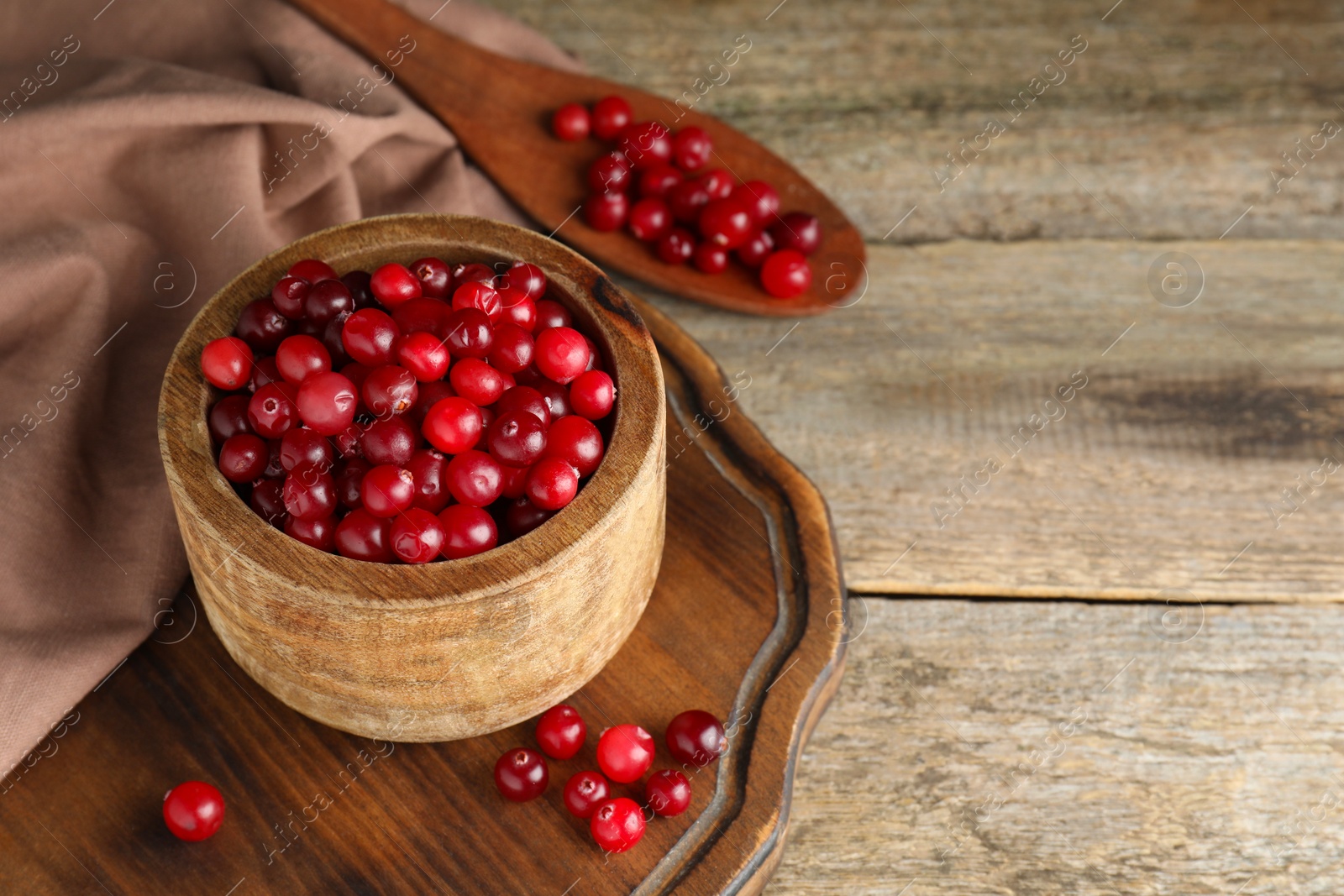 Photo of Cranberries in bowl and spoon on wooden table, space for text