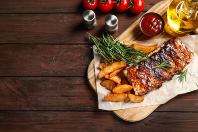 Delicious grilled ribs and garnish on wooden table, flat lay. Space for text