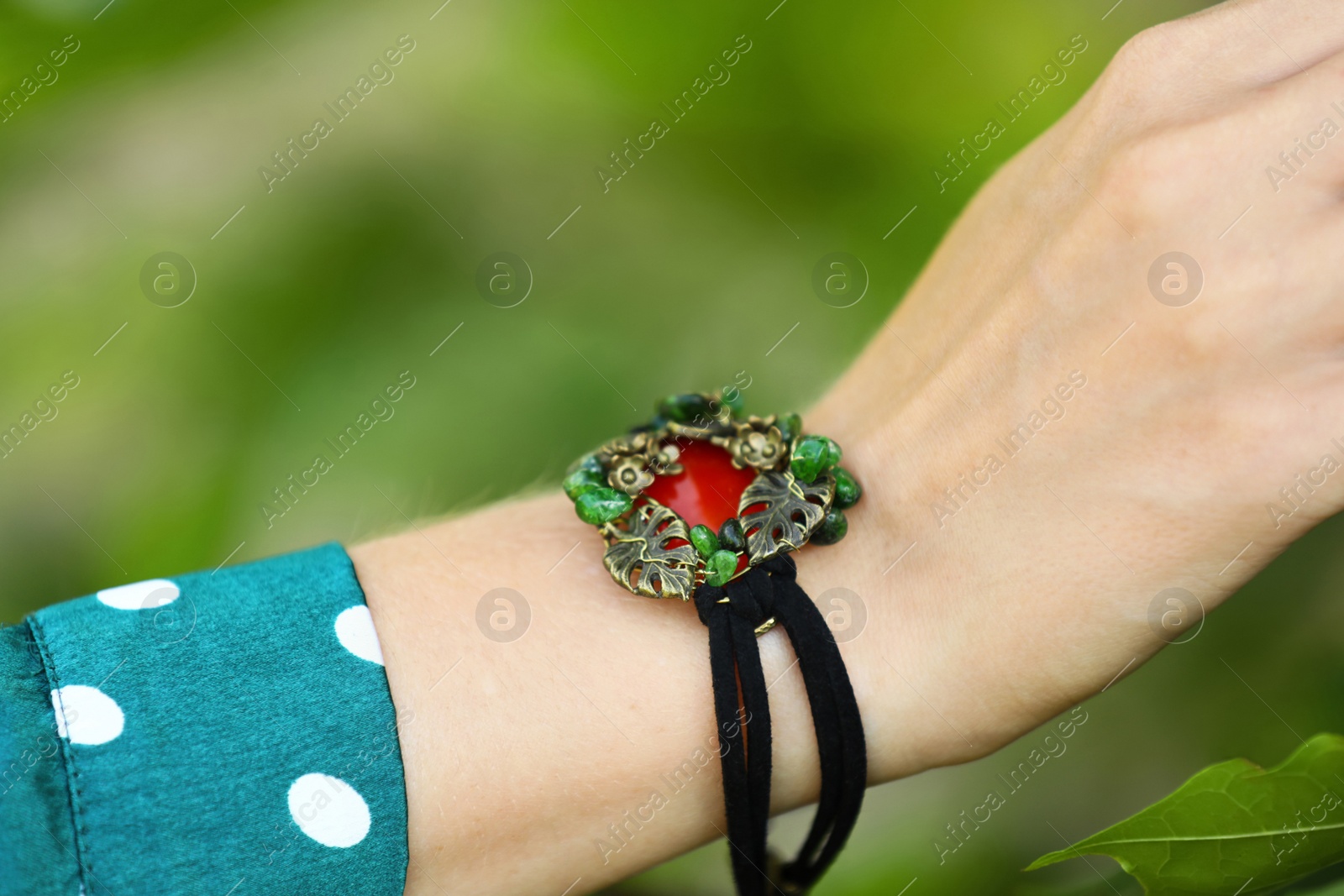 Photo of Young woman wearing beautiful metal bracelet with carnelian and gemstones outdoors, closeup