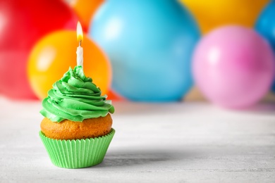 Photo of Delicious birthday cupcake with candle and blurred balloons on background