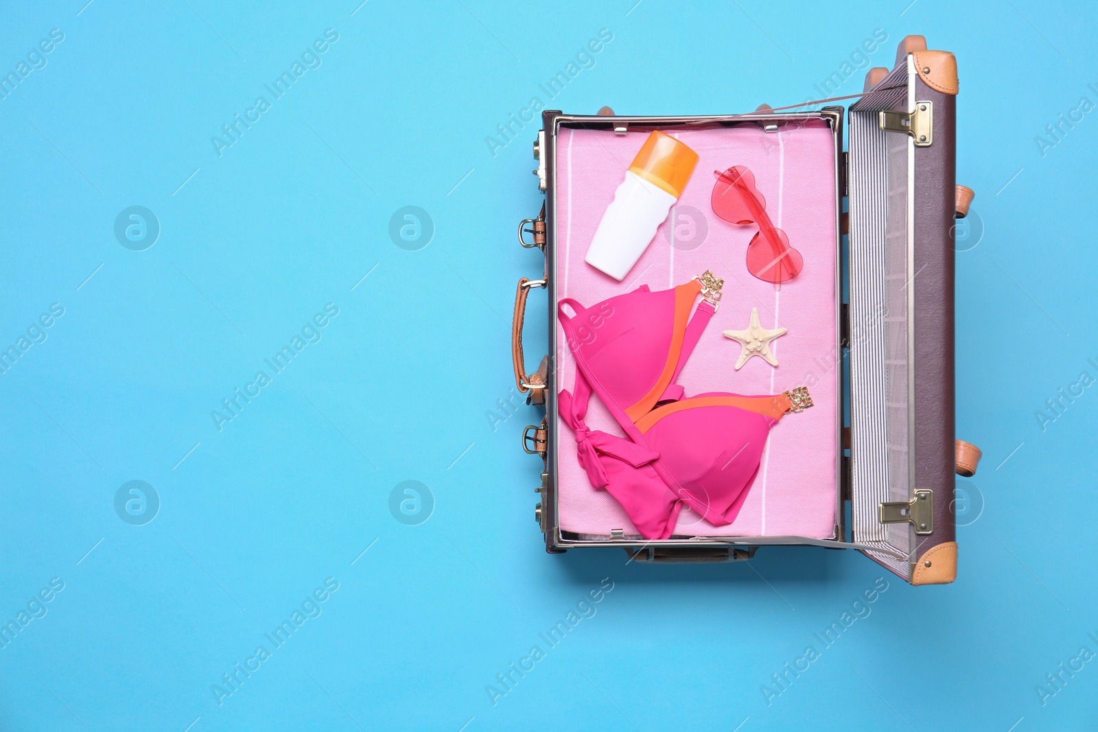 Photo of Open vintage suitcase with beach objects on blue background, top view. Space for text