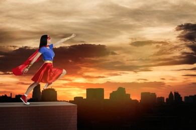 Image of Superhero, motivation and power. Woman in cape and mask on high building in city