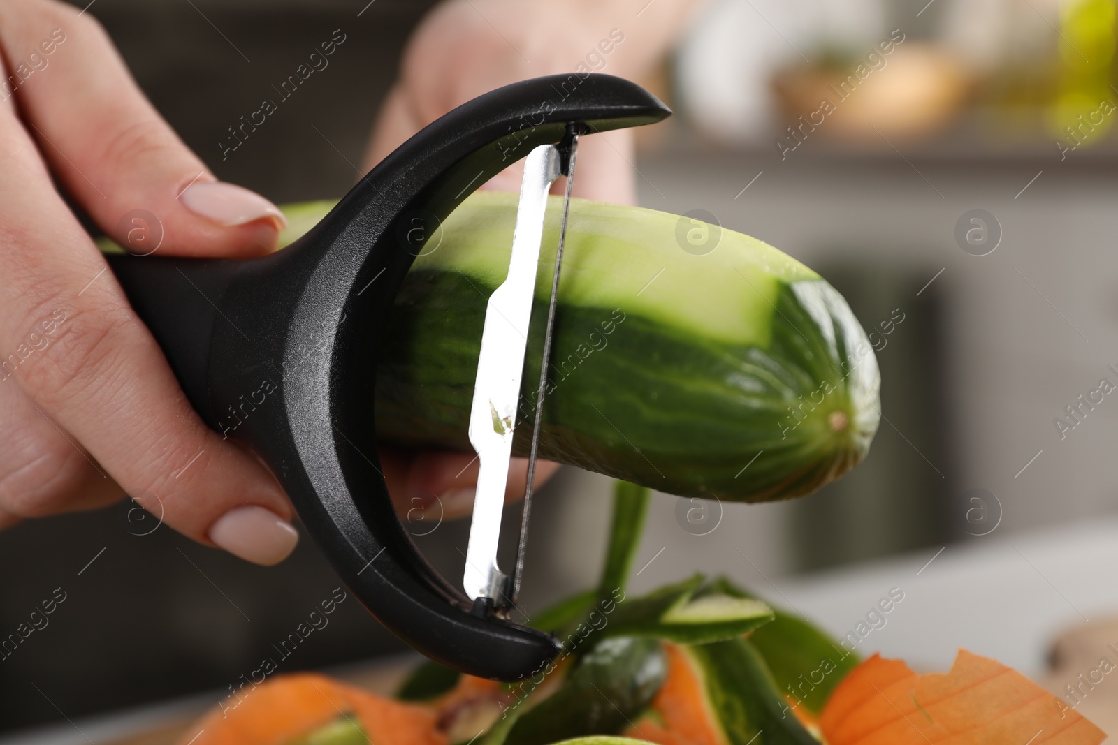 Photo of Woman peeling fresh cucumber at table indoors, closeup