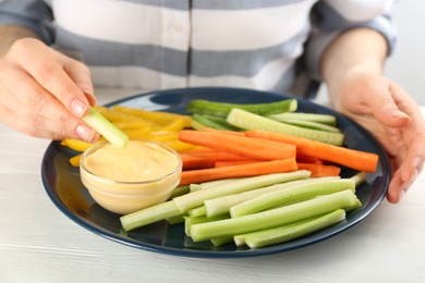 Woman dipping celery stick in sauce at white wooden table, closeup
