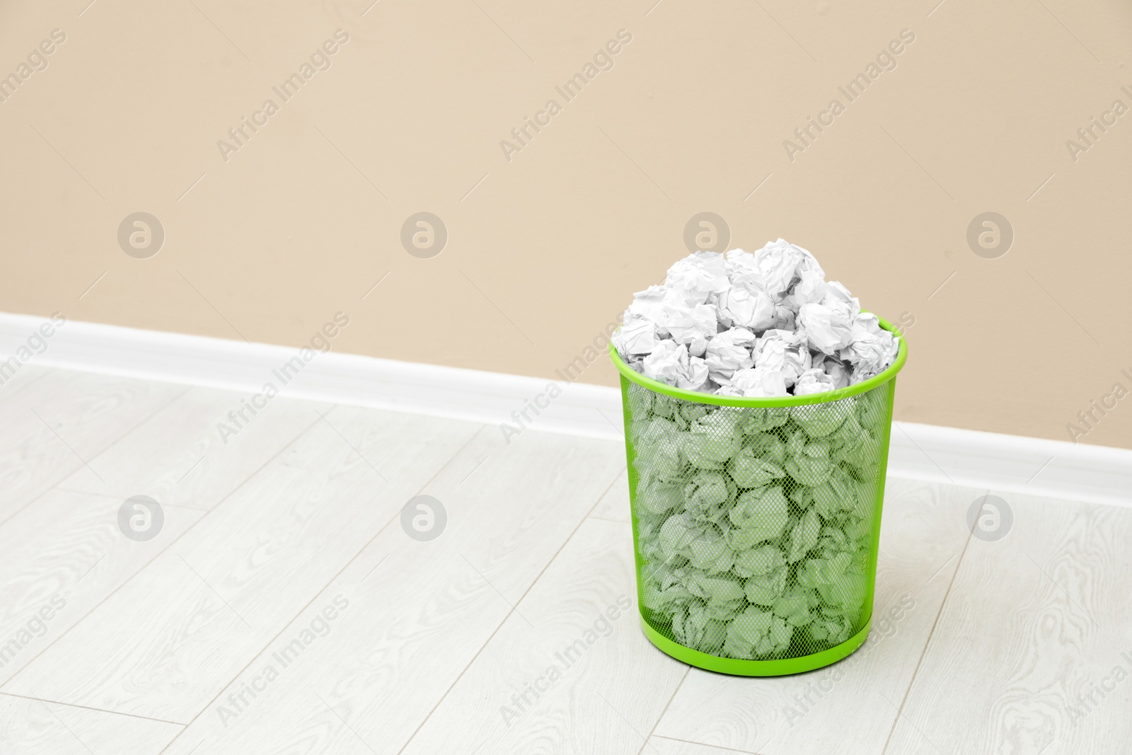 Photo of Metal bin with crumpled paper against color wall, space for text