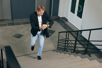Photo of Emotional man checking time while walking up stairs in office. Being late