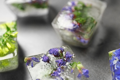 Ice cubes with flowers on grey stone table, closeup