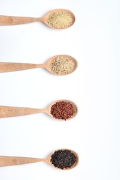 Spoons with different types of uncooked rice on white background, top view