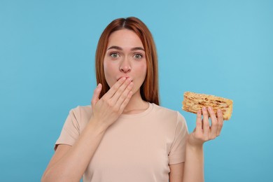 Photo of Emotional young woman with tasty cake on light blue background