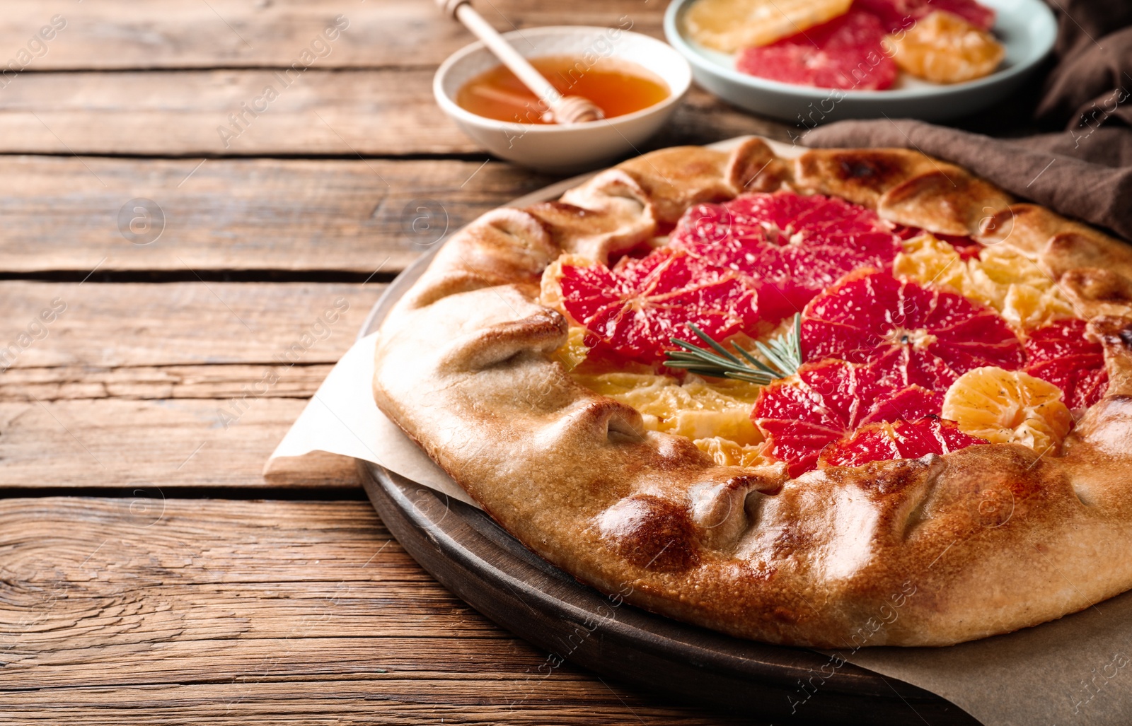 Photo of Tasty galette with citrus fruits and rosemary on wooden table, closeup