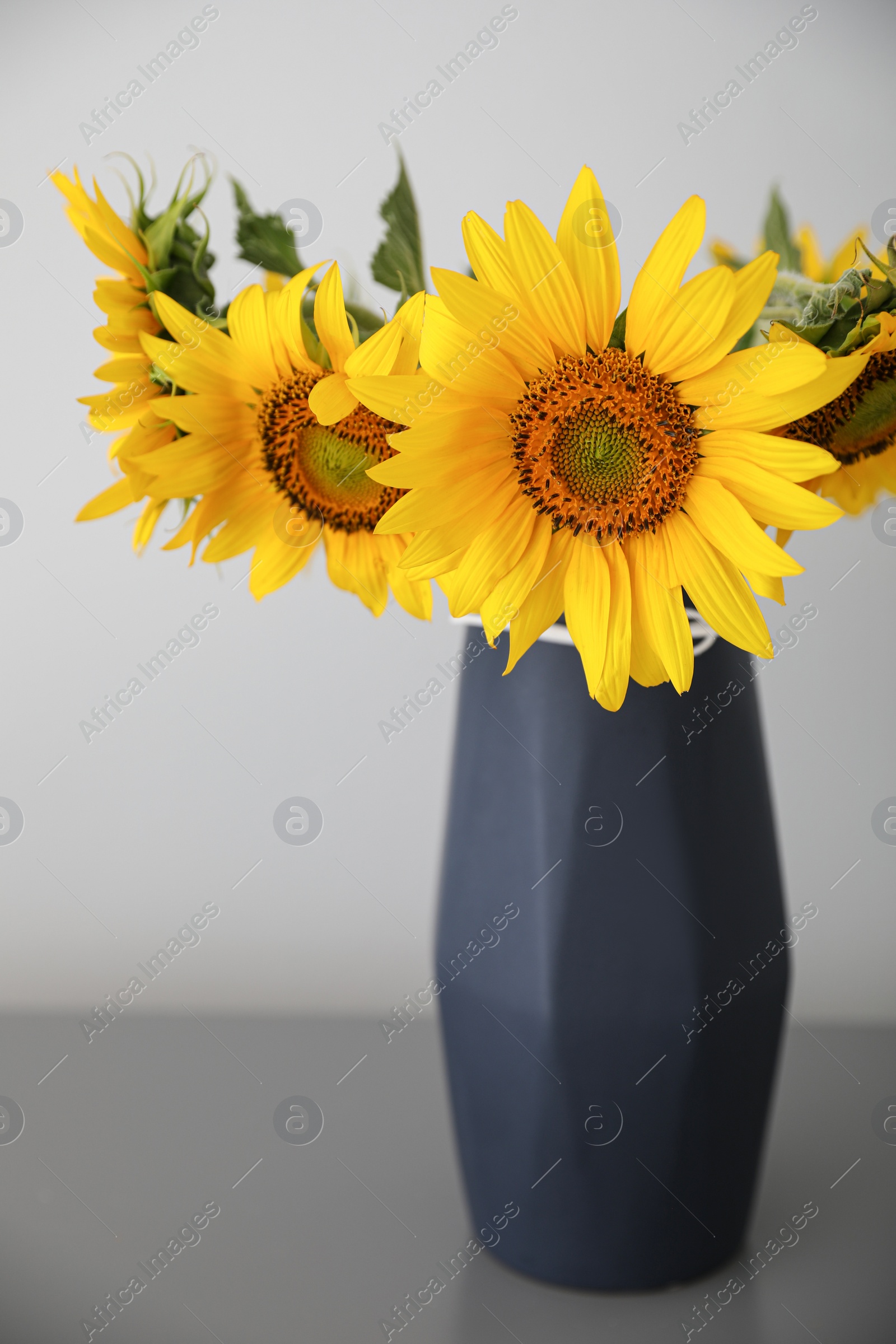 Photo of Bouquet of beautiful sunflowers on table near light wall