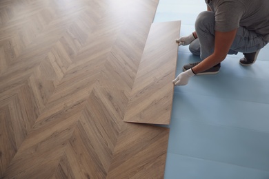 Worker installing laminated wooden floor indoors, closeup