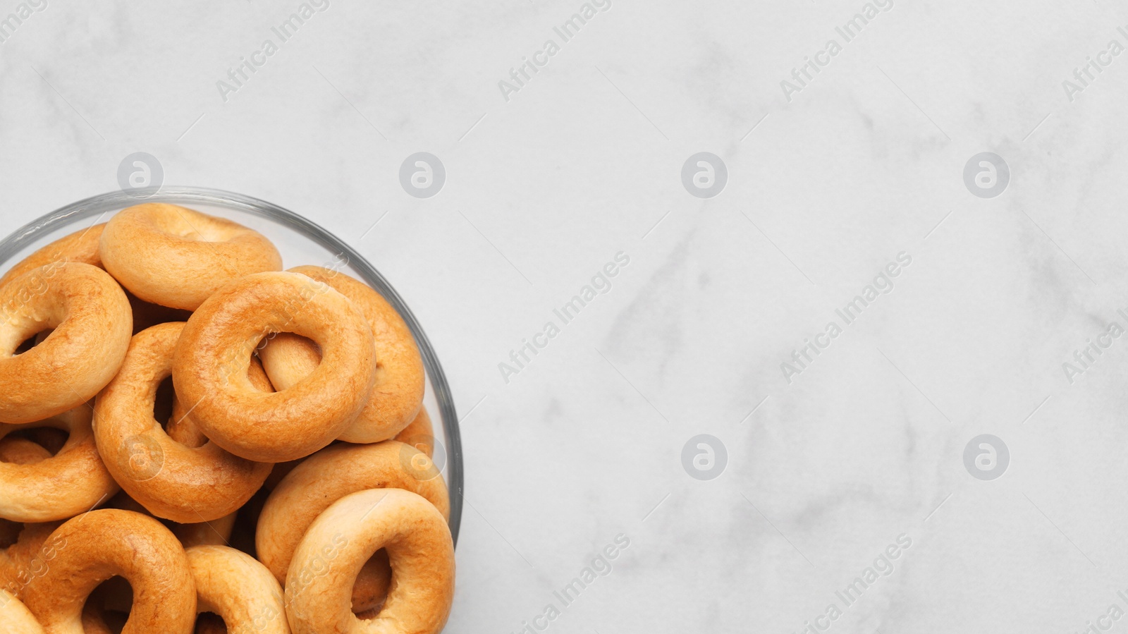 Photo of Bowl of tasty dry bagels (sushki) on white marble table, top view. Space for text