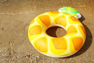 Photo of Bright inflatable pineapple ring on sandy beach near sea