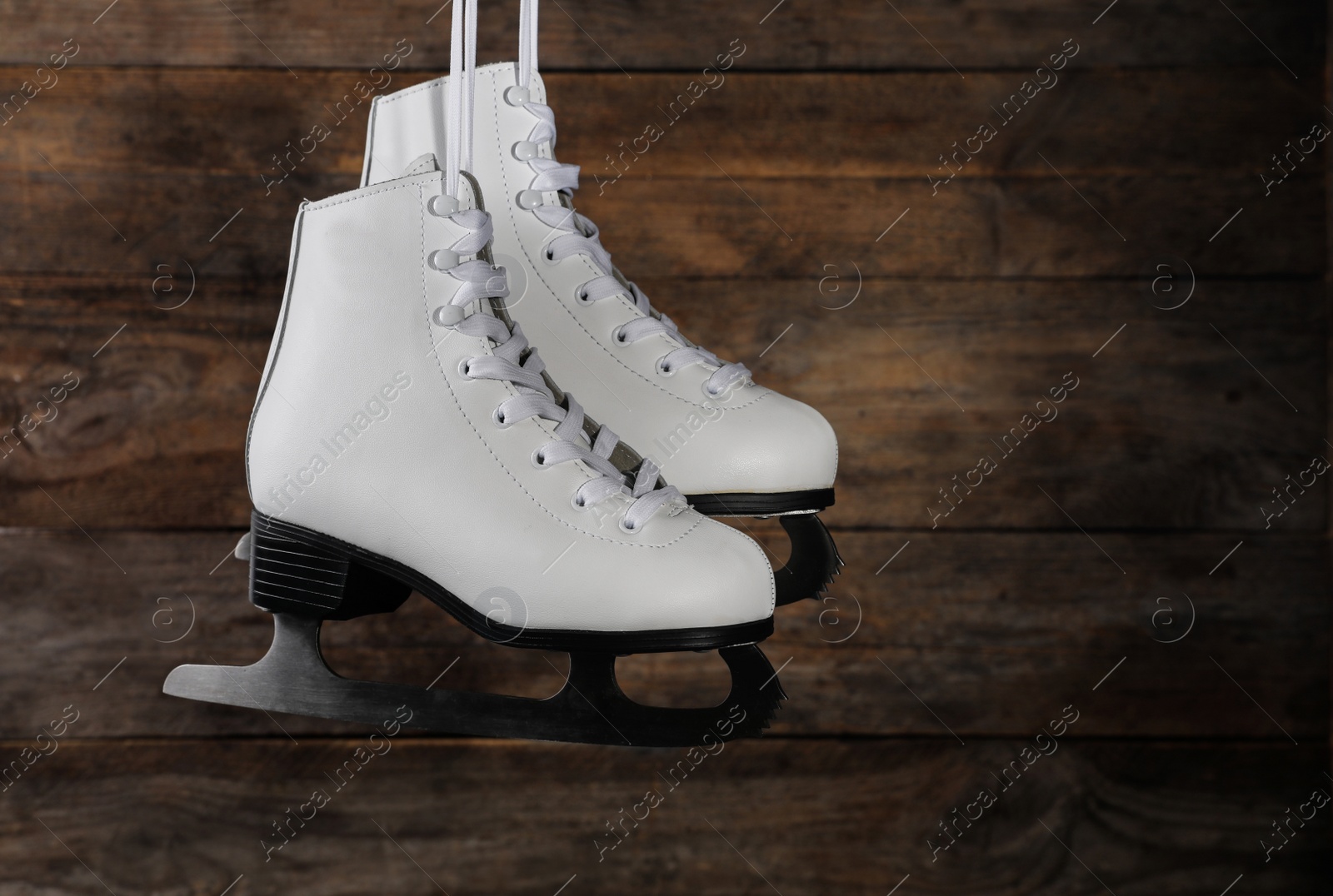 Photo of Pair of white ice skates hanging on wooden background. Space for text