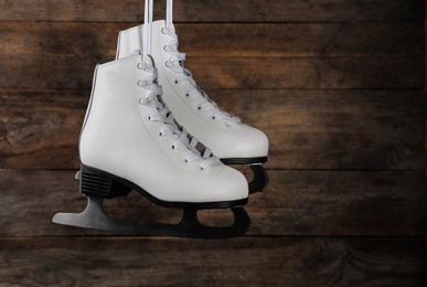 Photo of Pair of white ice skates hanging on wooden background. Space for text