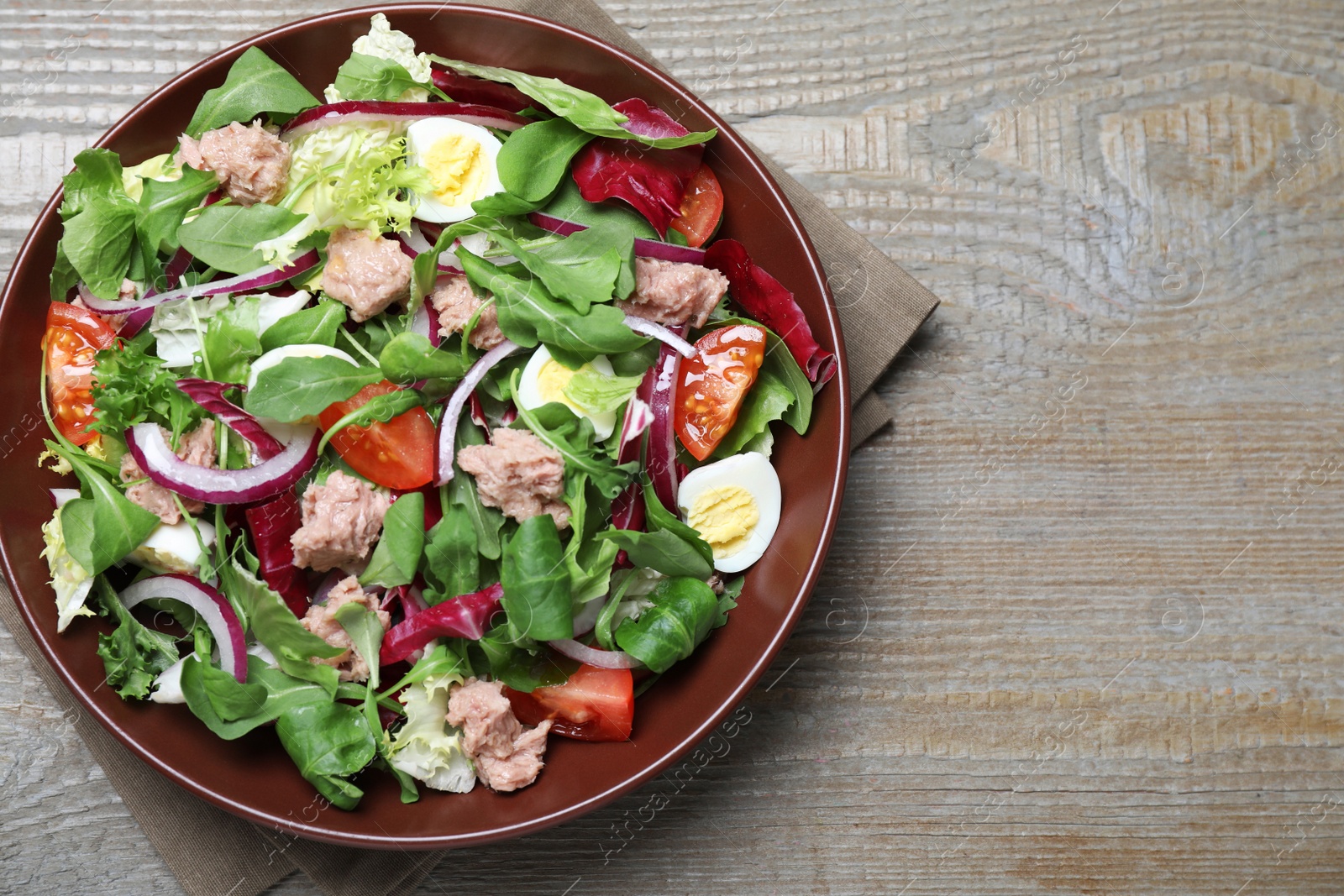 Photo of Bowl of delicious salad with canned tuna and vegetables on wooden table, top view. Space for text